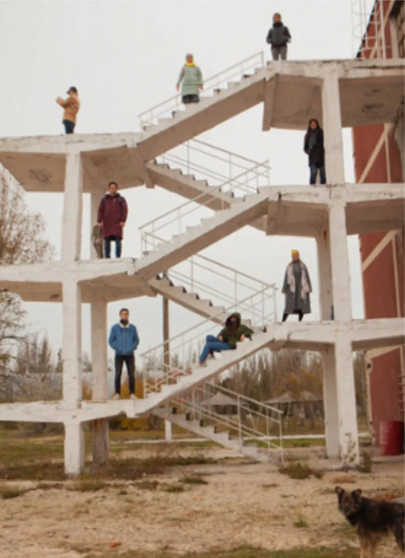 A group of people standing and sitting on various levels of an outdoor, unfinished concrete staircase.