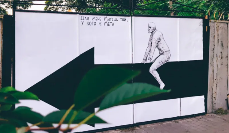 Painting of an outdoor mural in a public space featuring a person sitting on an arrow pointing leftwards.