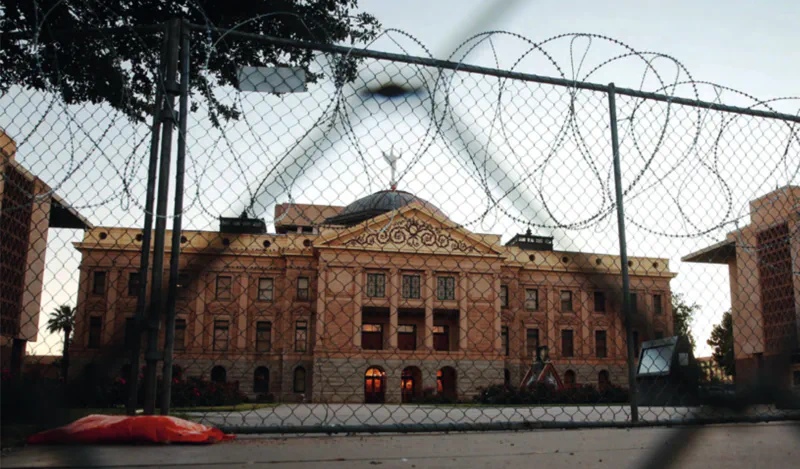 A grand municipal building behind a barbed wire fence
