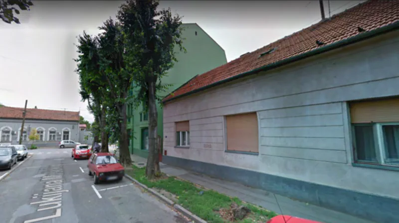 A street view of a residential area with medium-sized buildings, surrounded by sparse trees, captured during daylight.