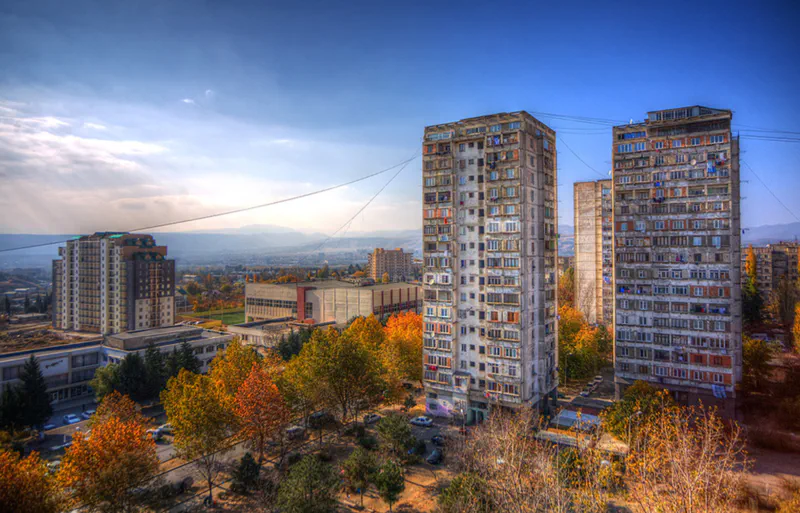 A view of a residential area with high-rise buildings surrounded by trees, taken in daylight with hills in the background.