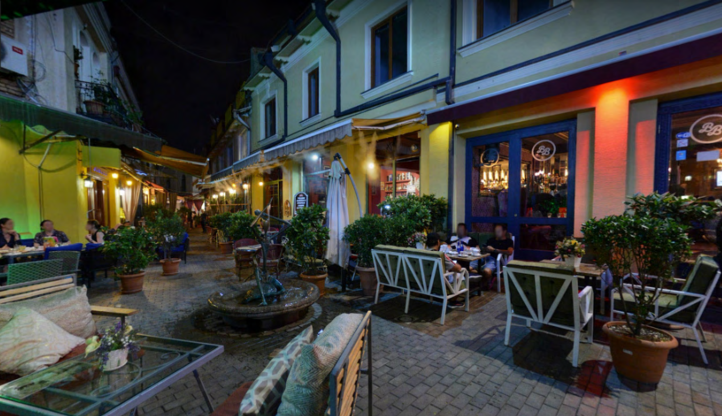 A dimly lit street in Tbilisi with small shops and outdoor seating areas under artificial lights.