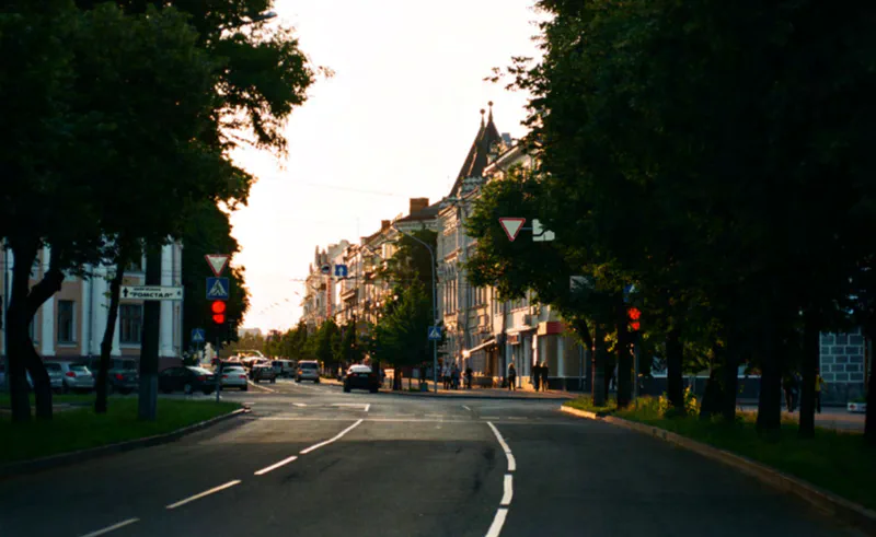 A busy urban crossroad lined with trees on both sides and multiple cars moving through intersections.